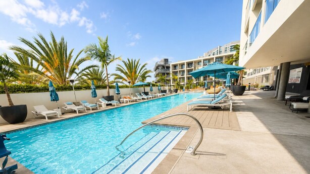 A swimming pool with lounge chairs and umbrellas, surrounded by palm trees and a building with balconies. - Marine Life: Smell the Sea, Feel the Breeze (Marina del Rey)