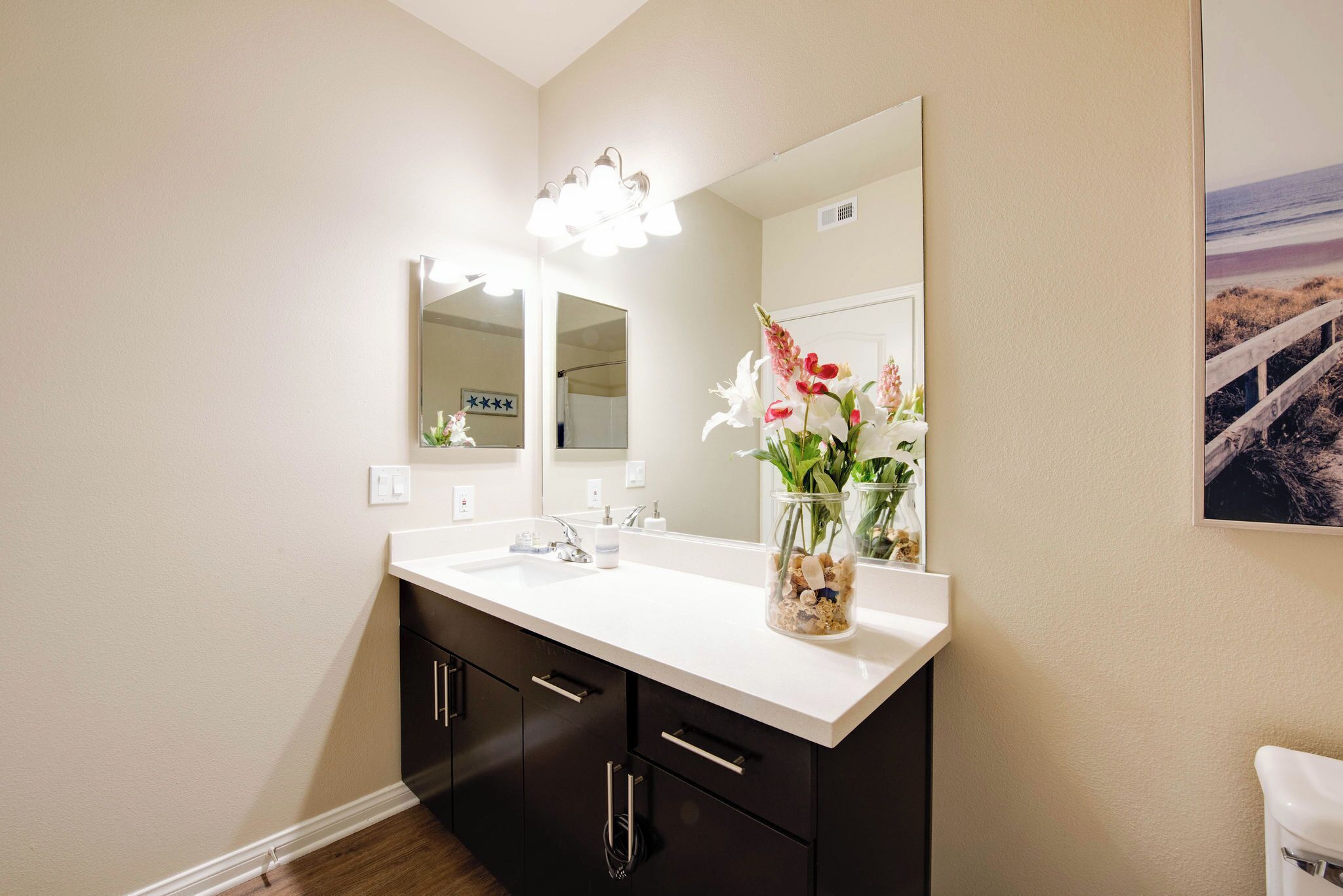 A bathroom with a white sink, black cabinets, a large mirror, and a vase with flowers.