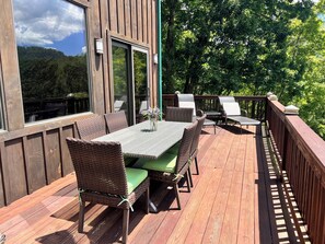 Une terrasse en bois, dotée de meubles en osier et d’une table, qui offre une vue sur une zone boisée.