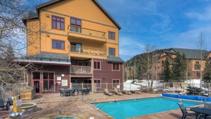 A multi-story building with a pool and hot tub area, outdoor seating, and a view of a mountainous landscape. - River Run Village |  Cozy 1BR for 6 | Pool Access (Keystone)