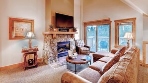A spacious living room with a stone fireplace, a flat-screen TV, a large sofa, and a balcony with outdoor furniture. - River Run Village |  Cozy 1BR for 6 | Pool Access (Keystone)