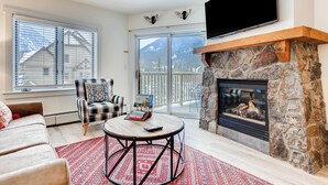 A cozy living room with a fireplace, a flat-screen TV, a comfortable sofa, and a view of mountains through the glass doors. - Keystone Escape | Pool Access | Close to the Lifts (Keystone)