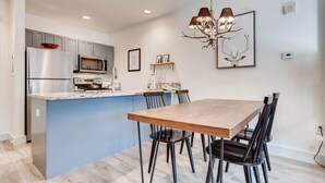 A modern kitchen with grey cabinets, a stainless steel refrigerator, a microwave, and a built-in oven. There is a wooden dining table with black chairs and a chandelier above. - Keystone Escape | Pool Access | Close to the Lifts (Keystone)