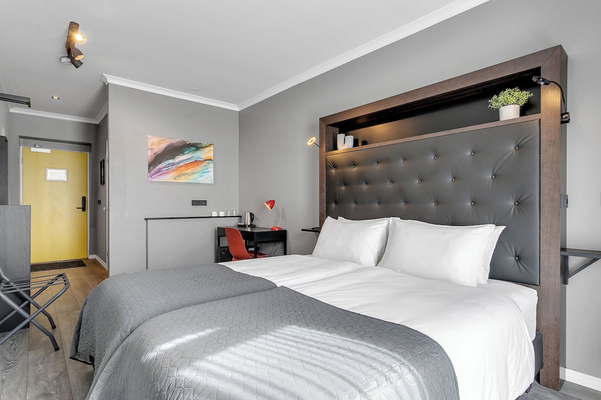 Ein modernes Hotelzimmer mit einem großen Bett, einem Schreibtisch und einem Stuhl. An der Wand hängt ein Gemälde und auf dem Schreibtisch steht eine Pflanze.