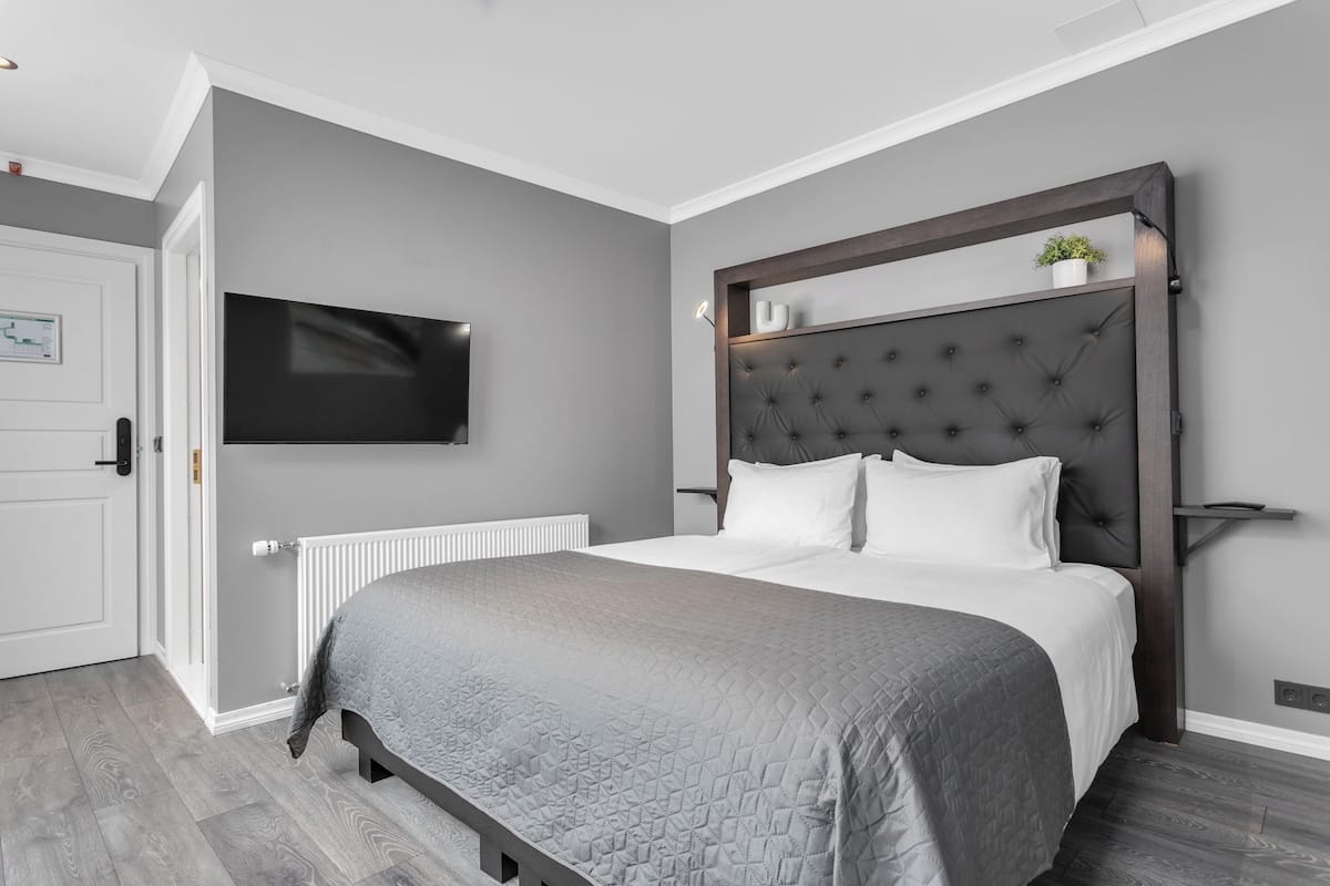 Ein modernes Schlafzimmer mit einer grauen gesteppten Bettdecke, einem gepolsterten Kopfteil, einem an der Wand montierten Fernseher und einer weißen Tür.
