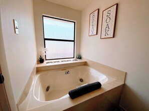 A bathroom with a bathtub, a window, and two framed words on the wall.