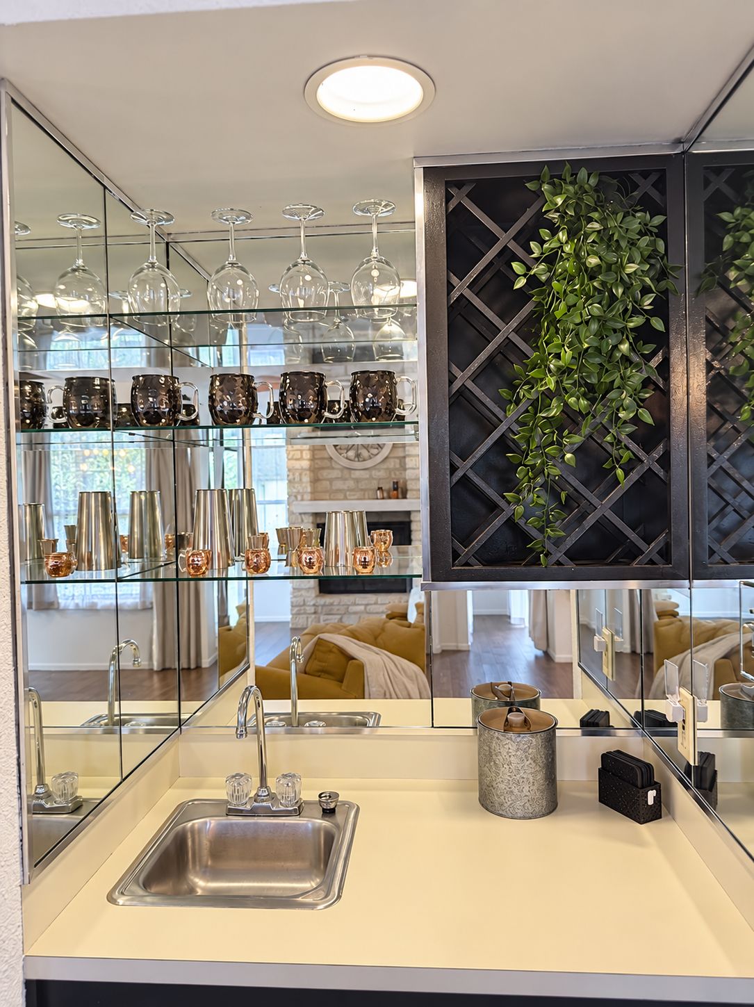 A modern kitchen with a large mirror, a sink, and a glass display of kitchenware.