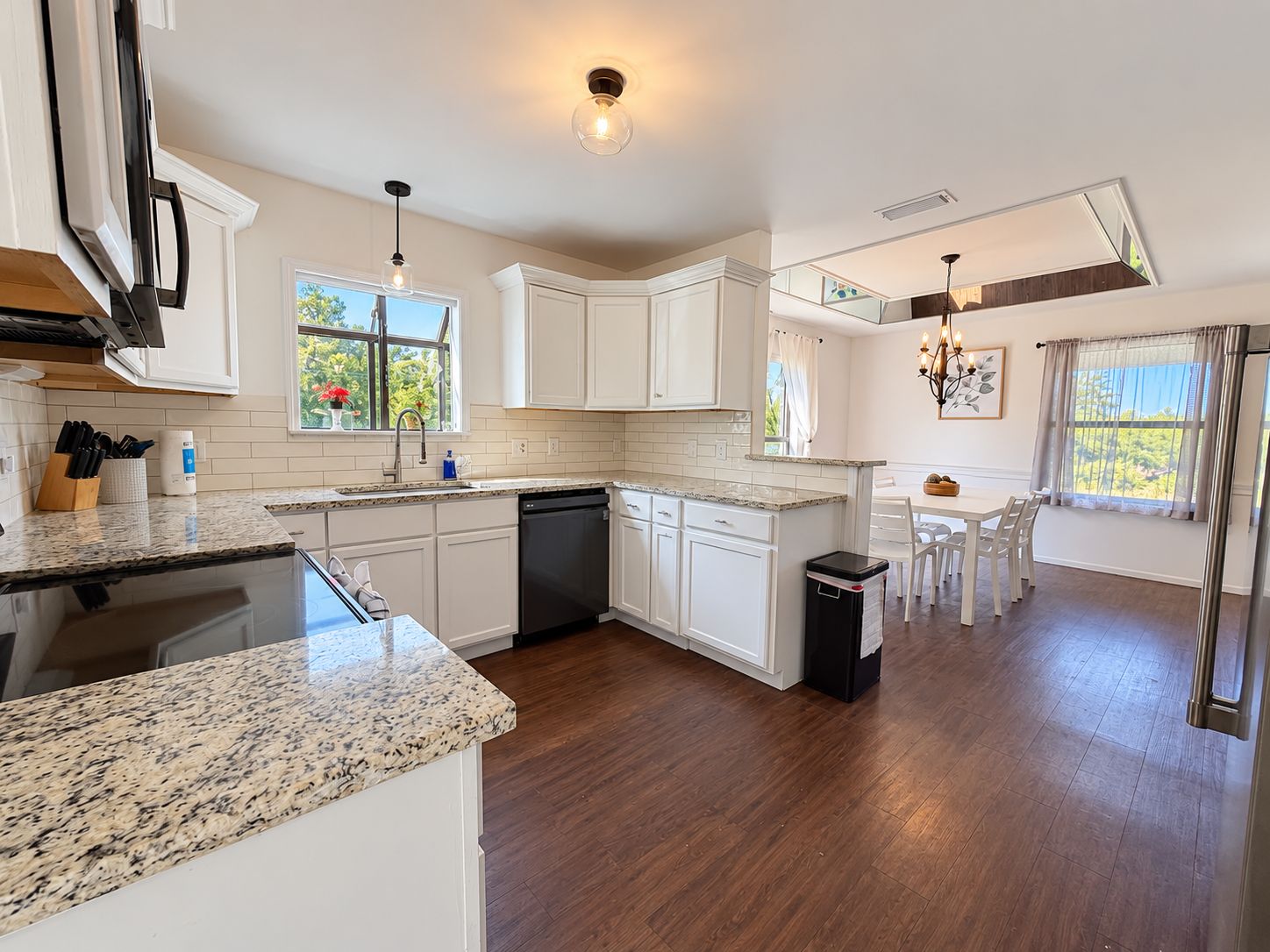 A modern kitchen with granite countertops, white cabinetry, and a dining area with a table and chairs.