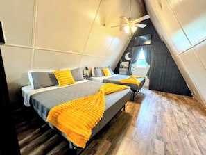 Quarto com duas camas, ventoinha no teto e janela com cortinas.