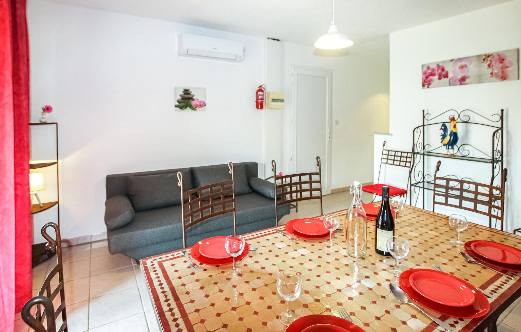A dining area with a tiled table set for four, a grey sofa, and a metal chair with a decorative rooster.