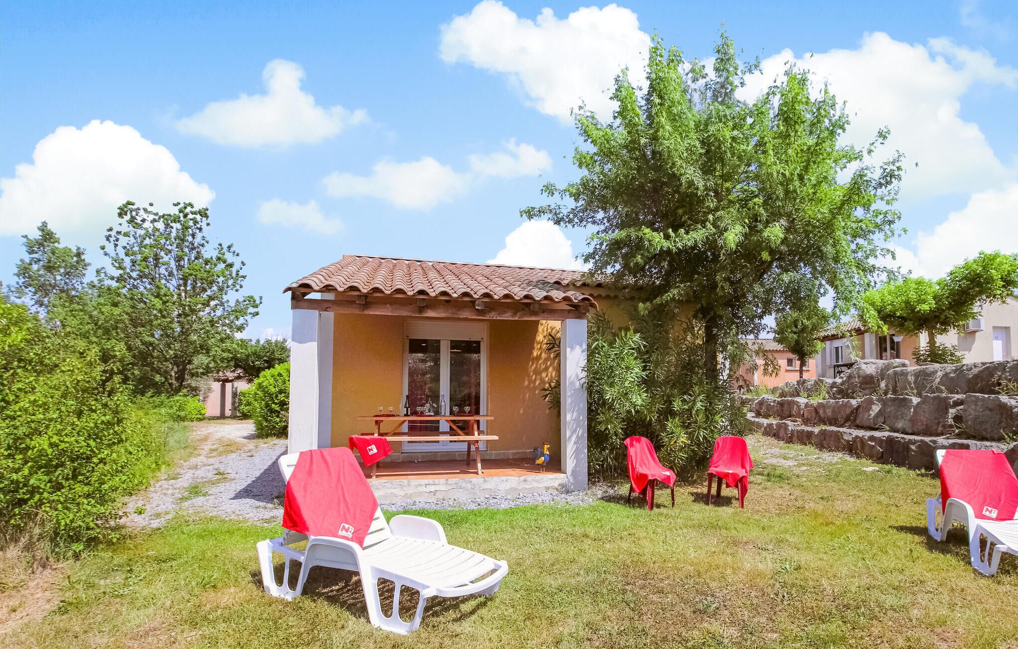 A small outdoor seating area with a table and chairs, a covered bench, and a stone wall in the background.