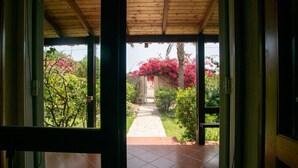 Une vue à travers une porte donnant sur un espace extérieur abrité, doté d’un sol carrelé, d’un chemin en pierre et d’une végétation luxuriante.
