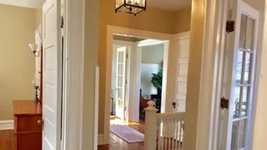 Un pasillo con suelo de madera, puertas blancas y una escalera con barandilla blanca.