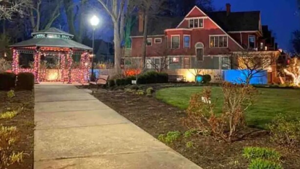 Un quiosco bien iluminado con luces colgantes, una casa de ladrillo rojo y un camino despejado que conduce a ella.