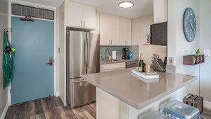 A modern kitchen with stainless steel appliances, a light blue door, and a clock on the wall.