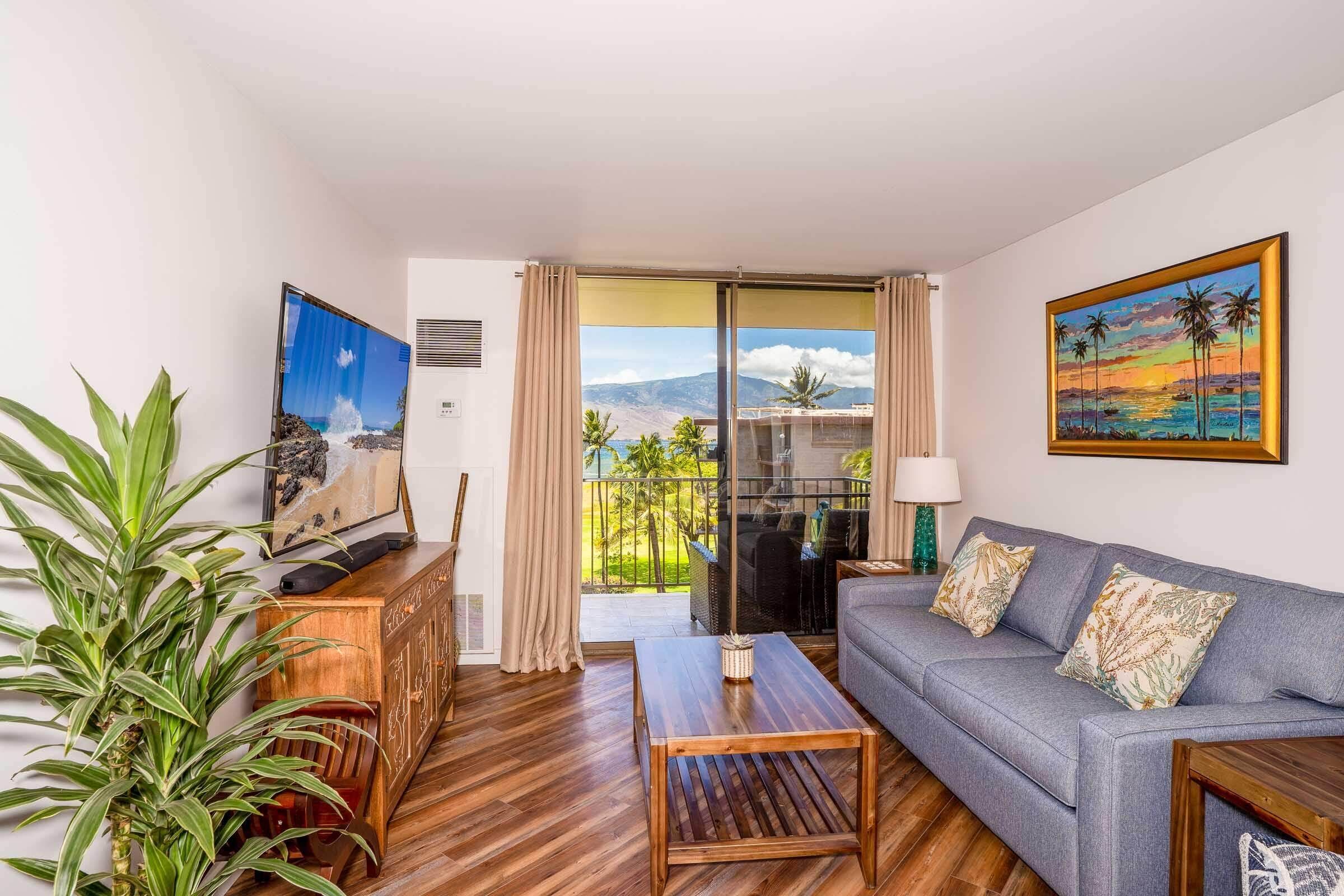 Un salon comprenant un canapé, une table basse, un téléviseur et un balcon offrant une vue sur les montagnes et les palmiers.