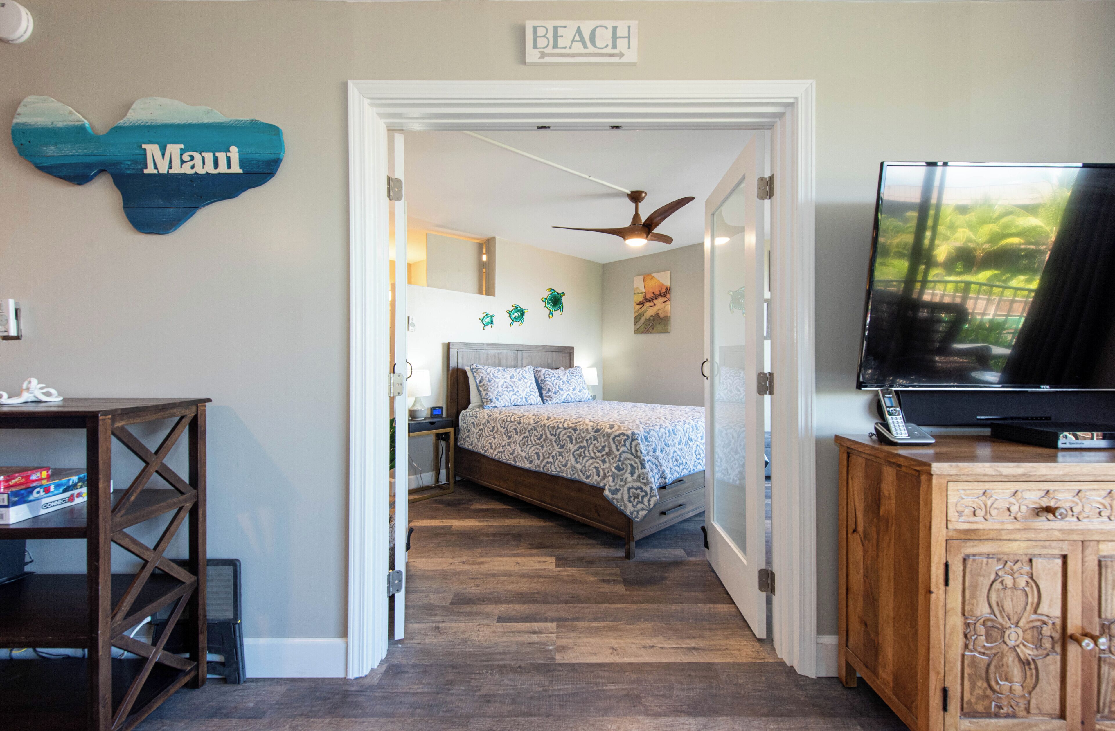 A bedroom with a bed, a TV, a wooden cabinet, and a wall sign reading 'Maui'.