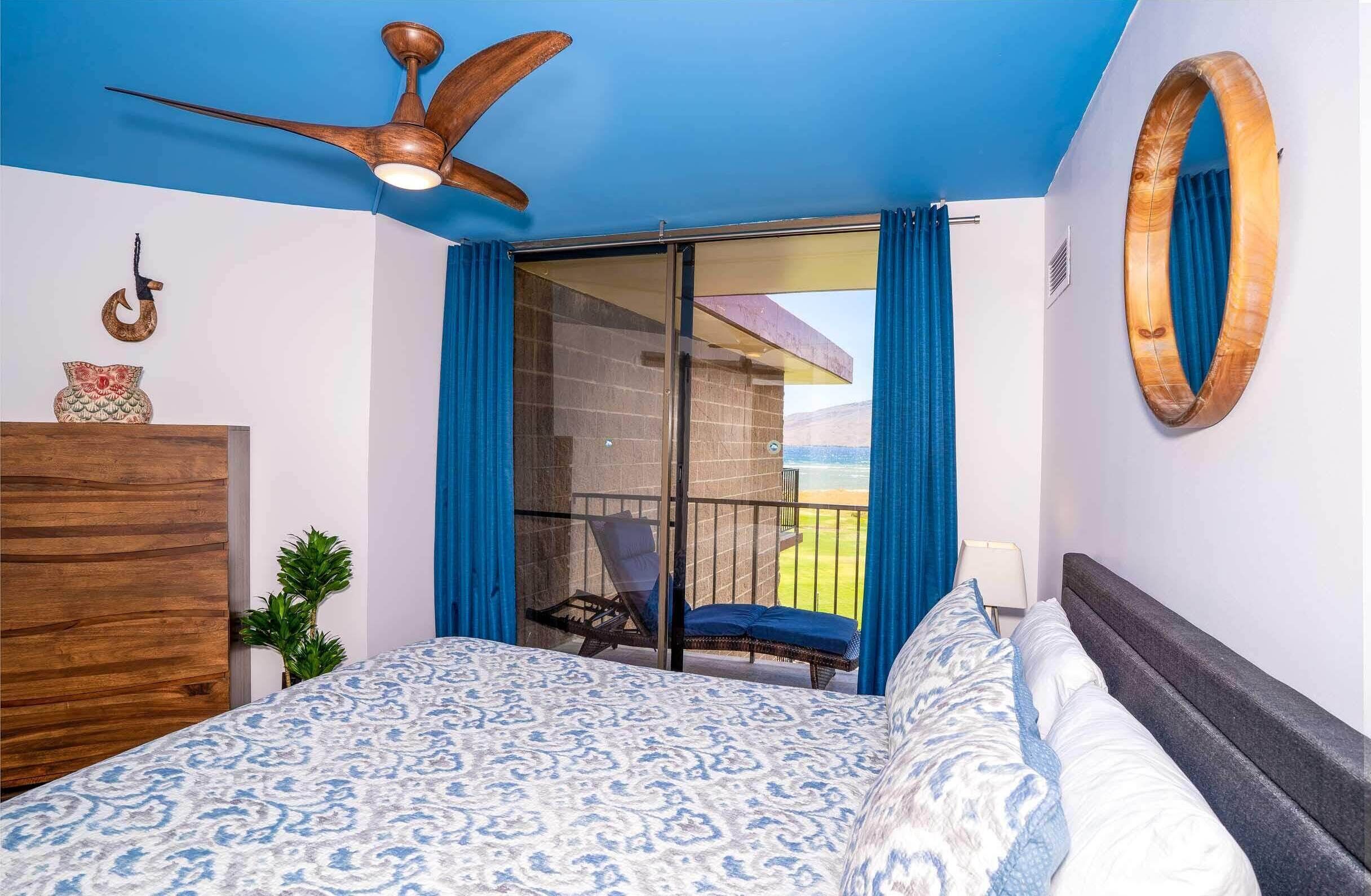 A bedroom with a bed, a ceiling fan, a chair by the window, and a view of the outdoors.