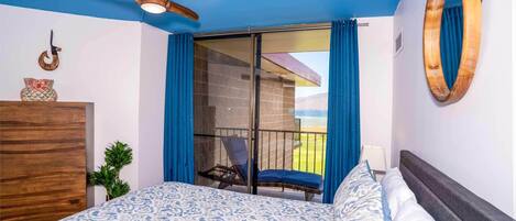 A bedroom with a bed, a ceiling fan, a chair by the window, and a view of the outdoors.