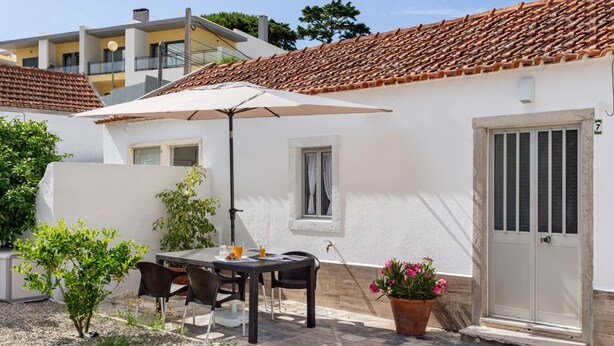 An outdoor patio with a table and chairs, a potted plant, and a door. - JOIVY Quaint house with Patio (Sintra)