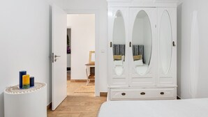 A bedroom with a white wardrobe, a bed, and a small table with candles. - JOIVY Quaint house with Patio (Sintra)