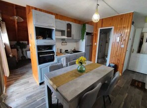A compact kitchen with wooden paneling, a dining table with chairs, and a hanging light fixture. - Superbe Loft Cocooning en Montagne Avec Balcon (Ustou)