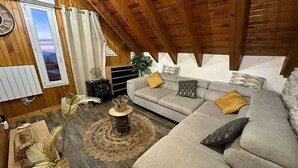 Ein gemütliches Wohnzimmer im Loft-Stil mit hohen Decken, einem grauen Sofa mit Kissen, einem runden Couchtisch und einem dekorativen Teppich.