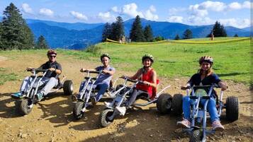 Four people on all-terrain vehicles in a grassy field with mountains in the background.