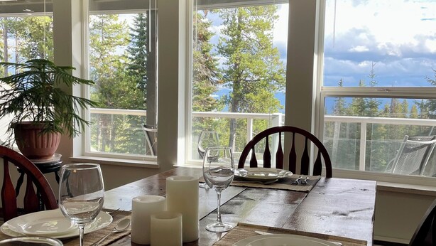 A dining table set with white plates, wine glasses, and candles, overlooking a mountainous landscape. - The Bear's Den Ski Chalet/Private Hot Tub/Ski In+Out/with Parking/Pet-Friendly! (Big White)