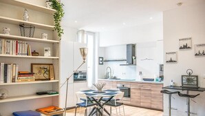 Una cocina moderna con comedor, piso de madera y una estantería llena de libros y objetos decorativos.