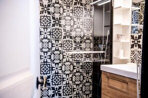 Une salle de bain avec des carreaux noirs et blancs formant un motif, un meuble en bois et une cabine de douche en verre.