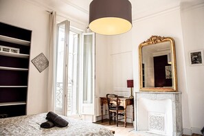 A bedroom with a bed, a desk, a chair, a large mirror, and a wardrobe.