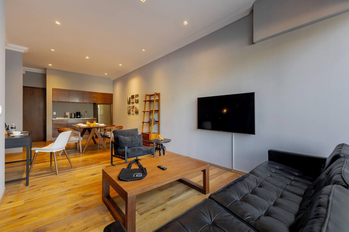 A modern living room with a black leather sofa, wooden coffee table, and a TV mounted on the wall.