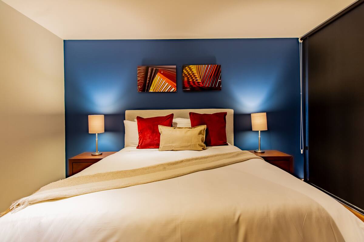 A hotel room with a bed, two nightstands, and two wall-mounted lamps.