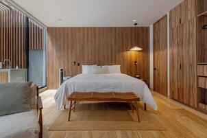 Un dormitorio moderno con una cama grande, paneles de madera, una mesita de noche y un banco.