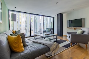 Una sala de estar moderna con un sofá gris, una mesa de centro y un televisor montado en la pared.