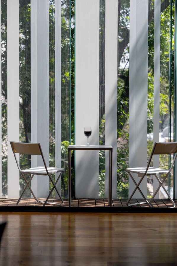 A room with a wooden floor, two chairs, a small table, and a glass of wine.