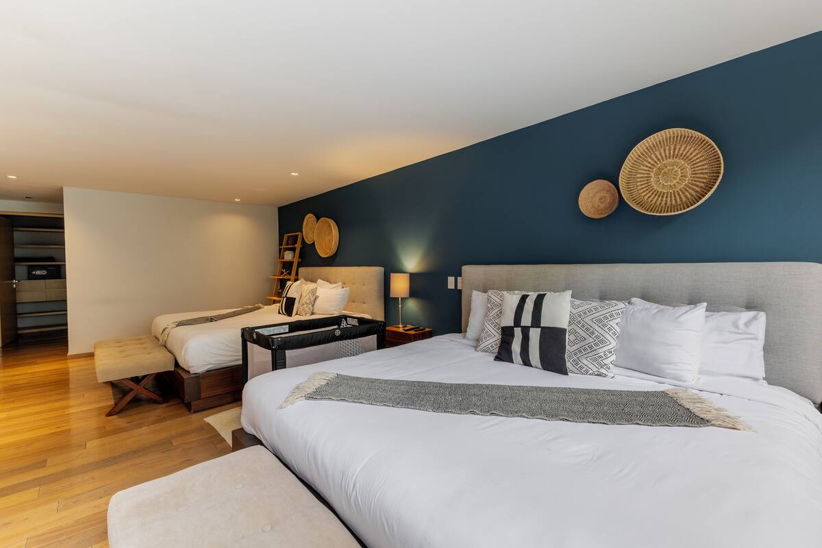 A modern bedroom with a large bed, bedside tables, a bench, and a view of a staircase.