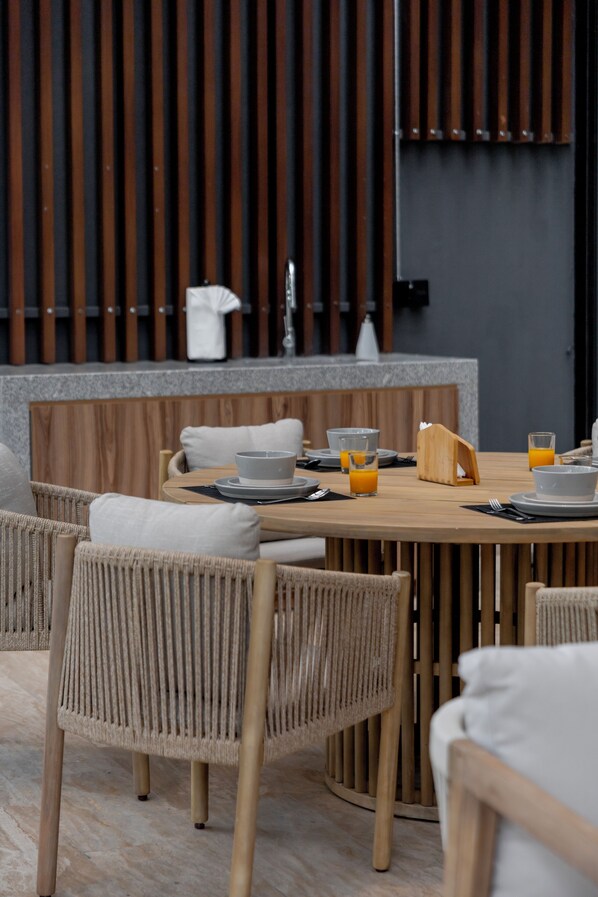A dining area with a round wooden table, wicker chairs, and a modern kitchen in the background.