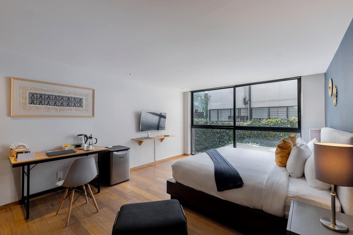 A modern hotel room with a large bed, a desk with a computer, a television, and a window offering a view of the outside.