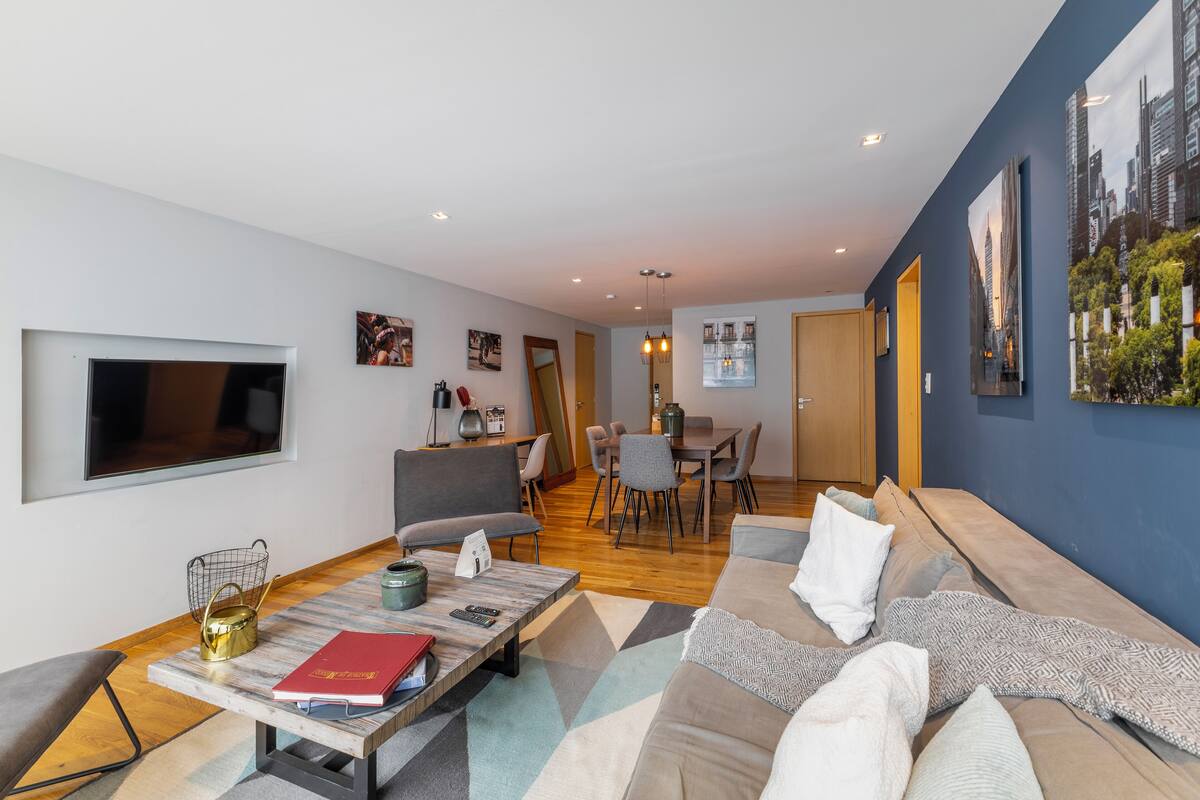 A modern living room with a sofa, a coffee table, and a dining area in the background.