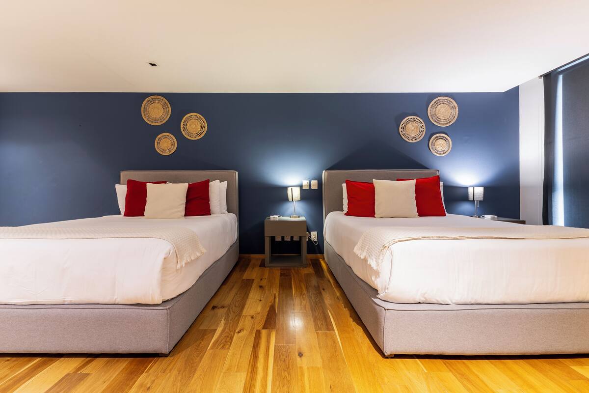 A hotel room with two beds, wooden flooring, and wall decor.