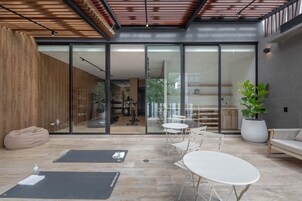 Un interior moderno con un vidrio que da a un comedor, una zona de estar con una mesa y sillas blancas, y una planta grande en maceta.