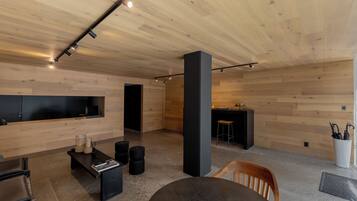 Un interior moderno con techo de madera, un sofá negro, una mesa redonda y un televisor montado en la pared.