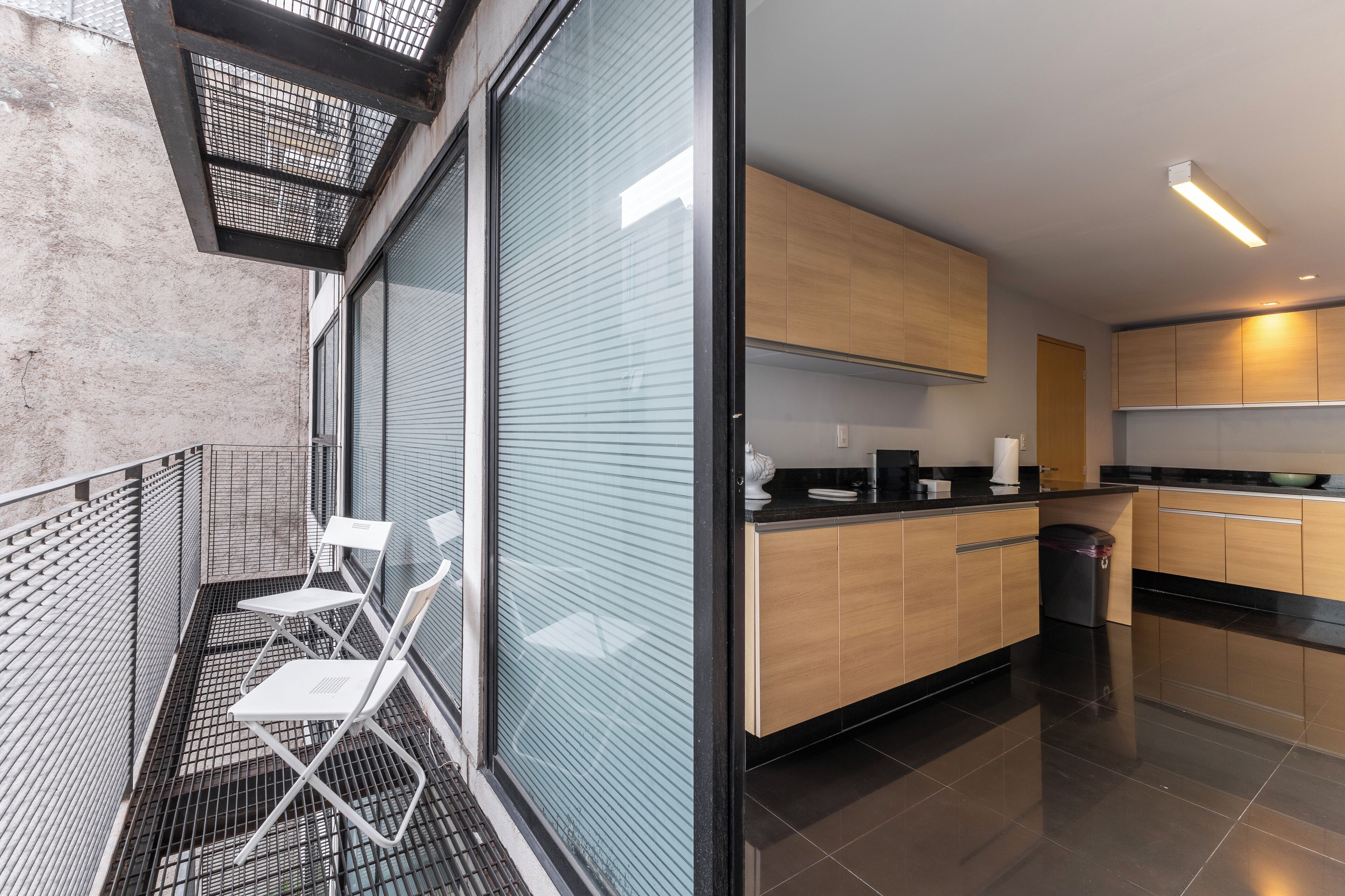 Une cuisine moderne avec des meubles en bois, un plan de travail noir et une petite poubelle.