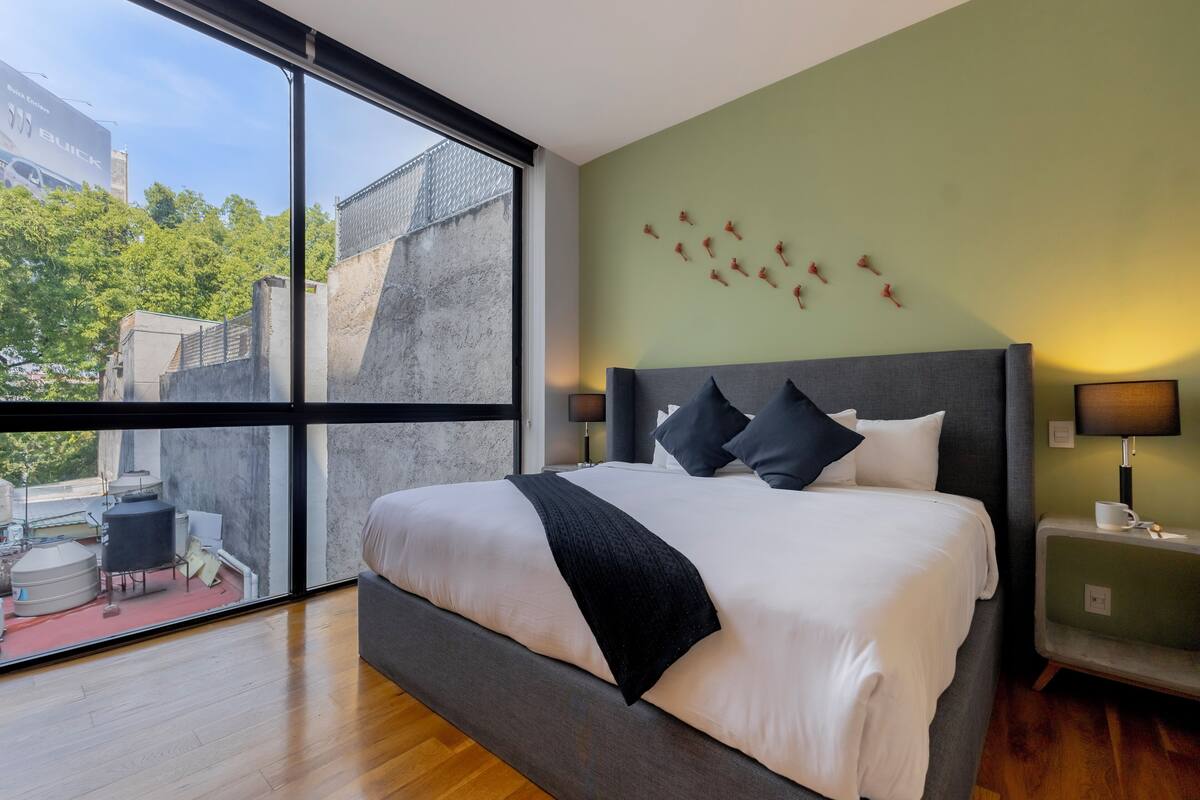 A modern hotel room with a large bed, a view of the city through floor-to-ceiling windows, and a minimalist decor.