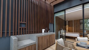Una cocina moderna con una isla integrada, paneles de madera y una puerta de vidrio que da a un dormitorio con cama y zona de estar.