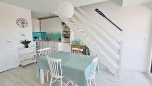 Una cocina moderna con armarios blancos, una mesa de comedor color turquesa y una escalera con una escoba apoyada contra la pared.