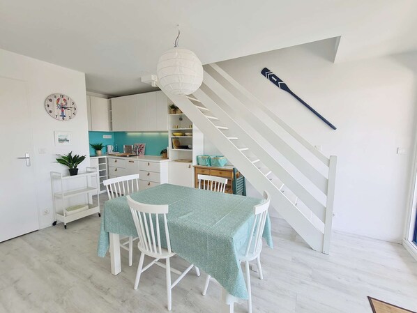 A modern kitchen with white cabinets, a teal dining table, and a staircase with a broom leaning against the wall. - Appartement en Duplex Avec vue Port Crouesty Pour Cinq Personnes (ARZON)