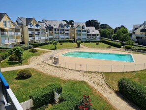 A residential building with a swimming pool surrounded by a sandy area and greenery.